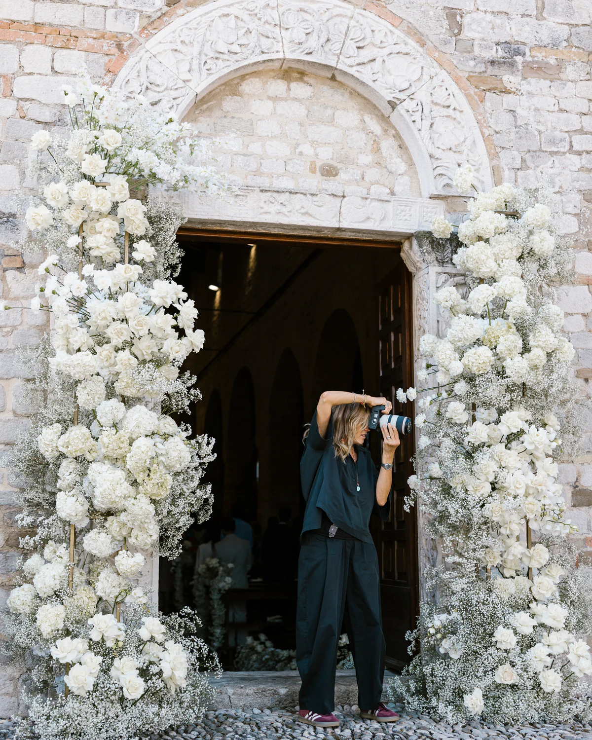 One of the two photographers taking a picture in a church doorway framed with white flowers