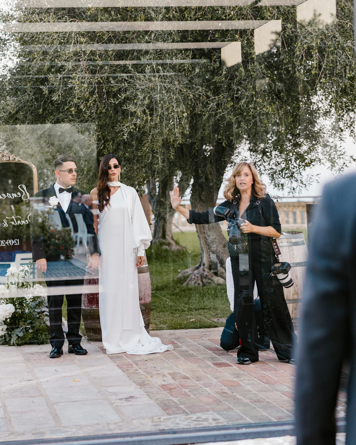 One of the two photographers directing the bride and groom, seen through a glass wall