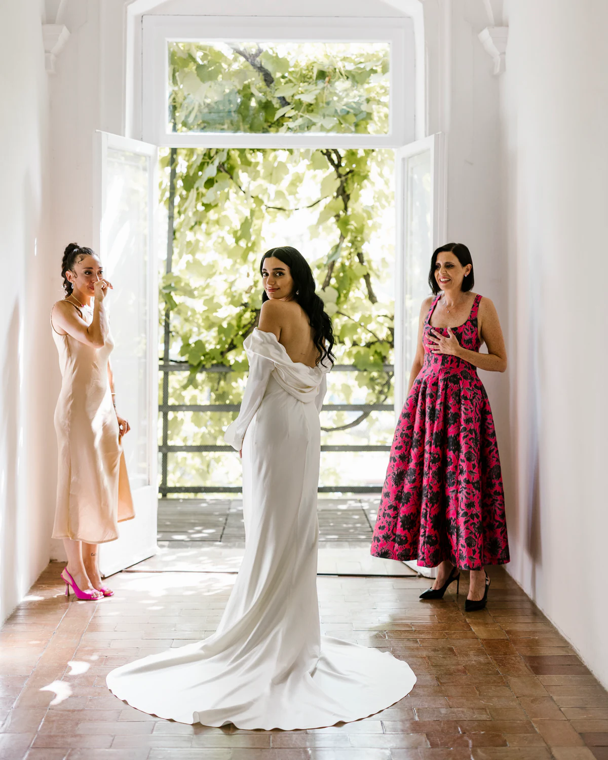 A bride looking back over her shoulder in an open doorway, between two friends