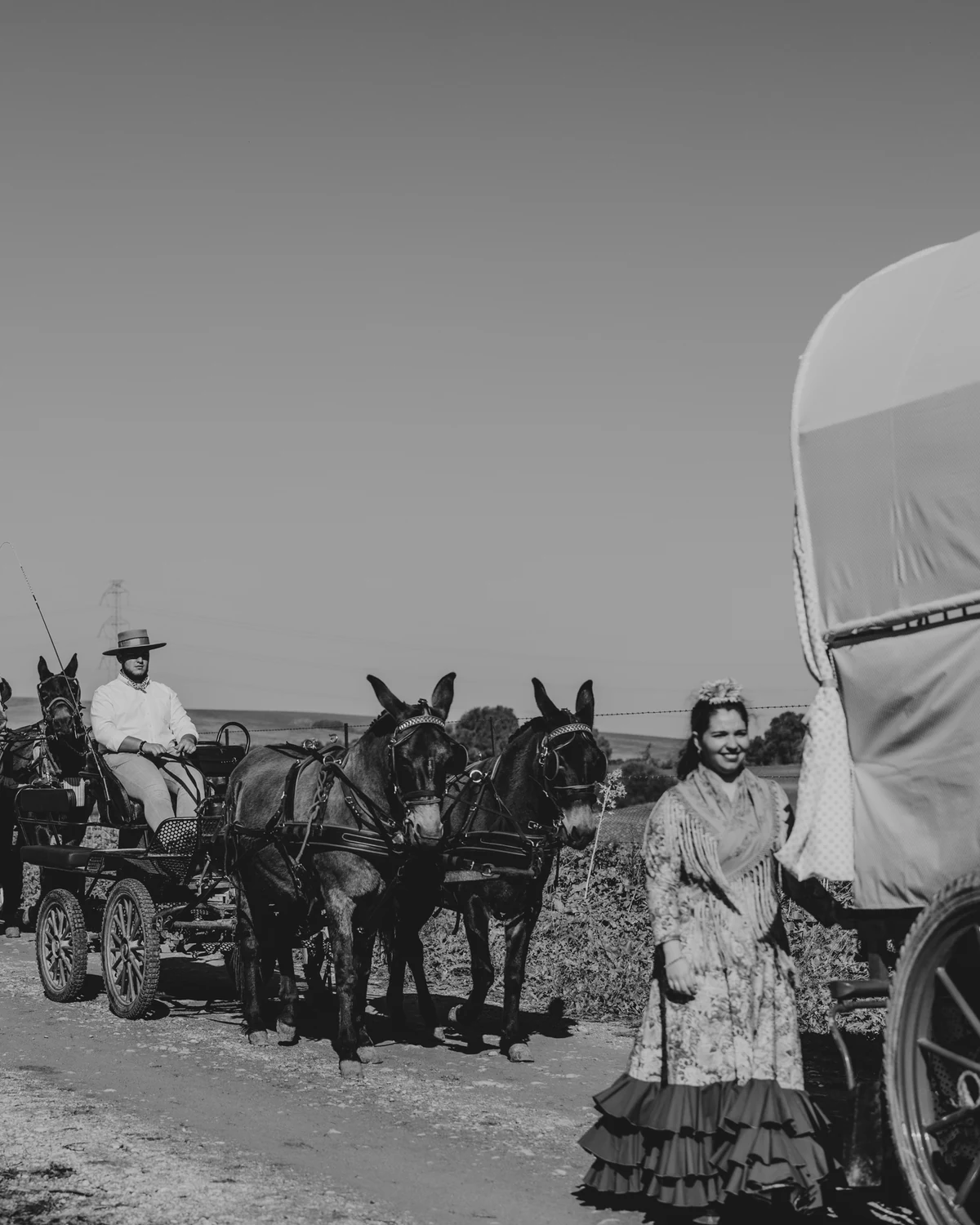 A mule-drawn cart and a woman in a flamenco dress beside a covered wagon, in black and white