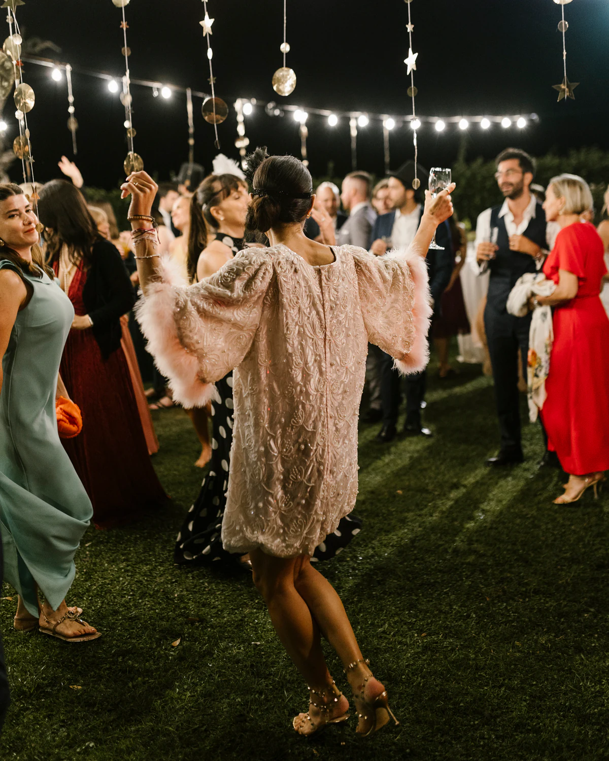 A woman dancing in an embellished coat at a night party under string lights