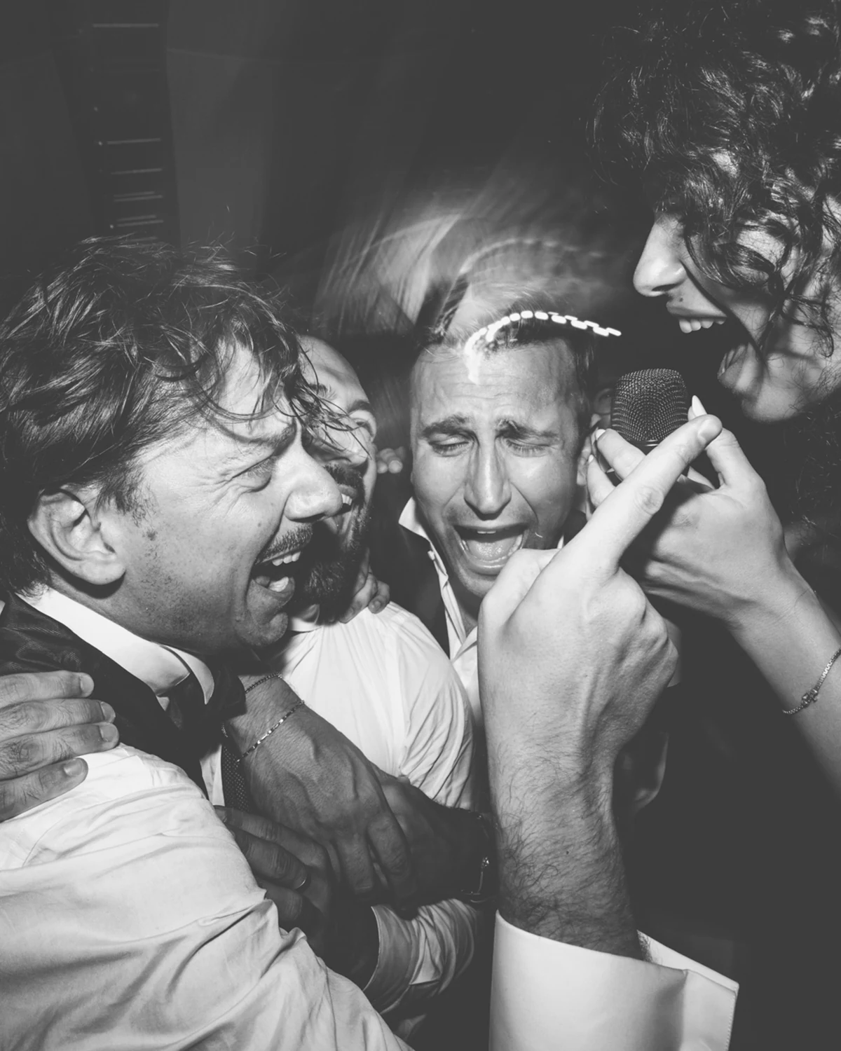 Guests singing together into a microphone, in black and white