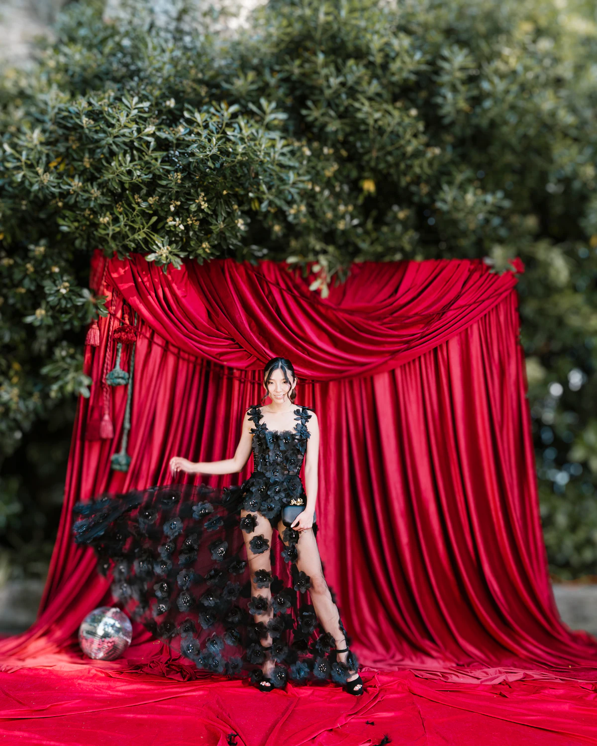 A woman in a black gown in front of a red velvet curtain in a garden