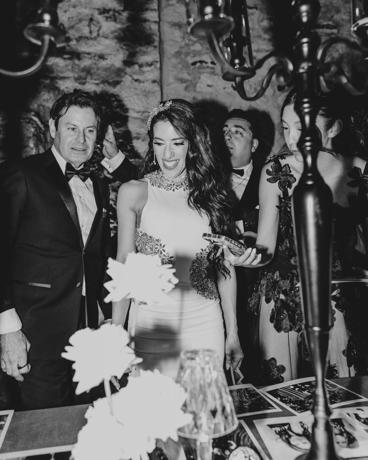 A bride smiling among guests beside a candelabra, in black and white