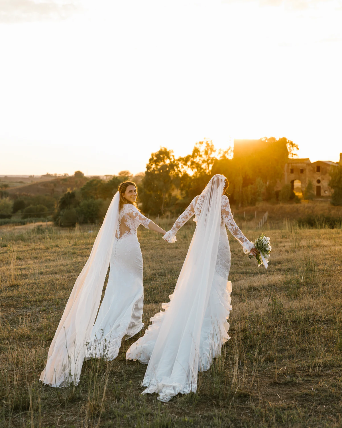 Two brides walking hand in hand through a field at sunset