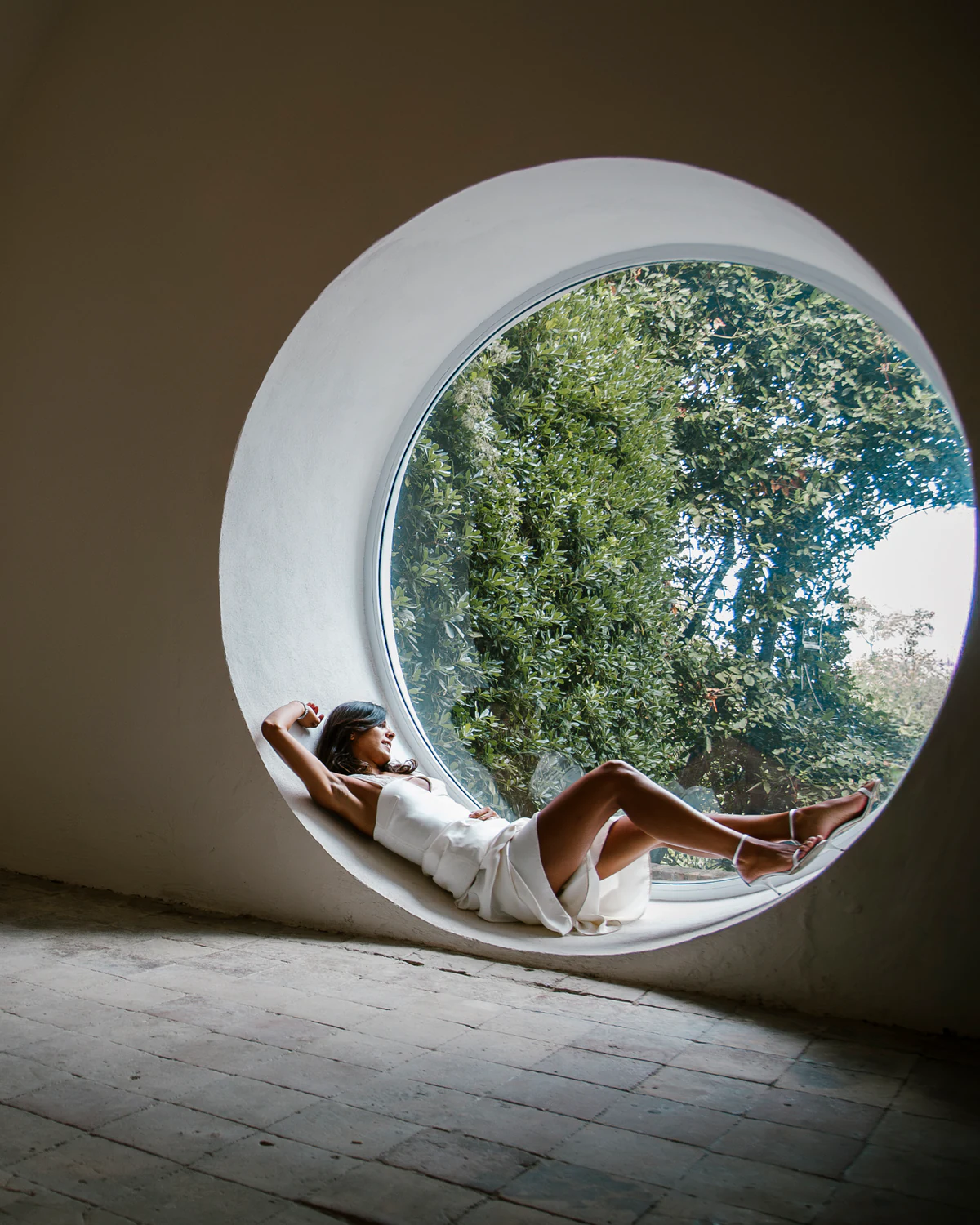 A woman lying inside a round window that frames the trees