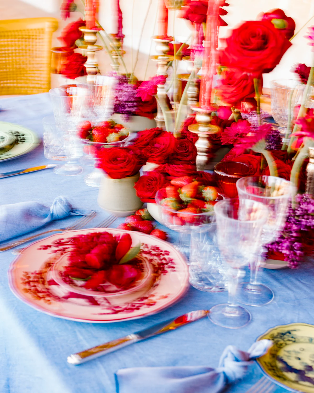 A table set with red flowers, pink plates and a blue cloth