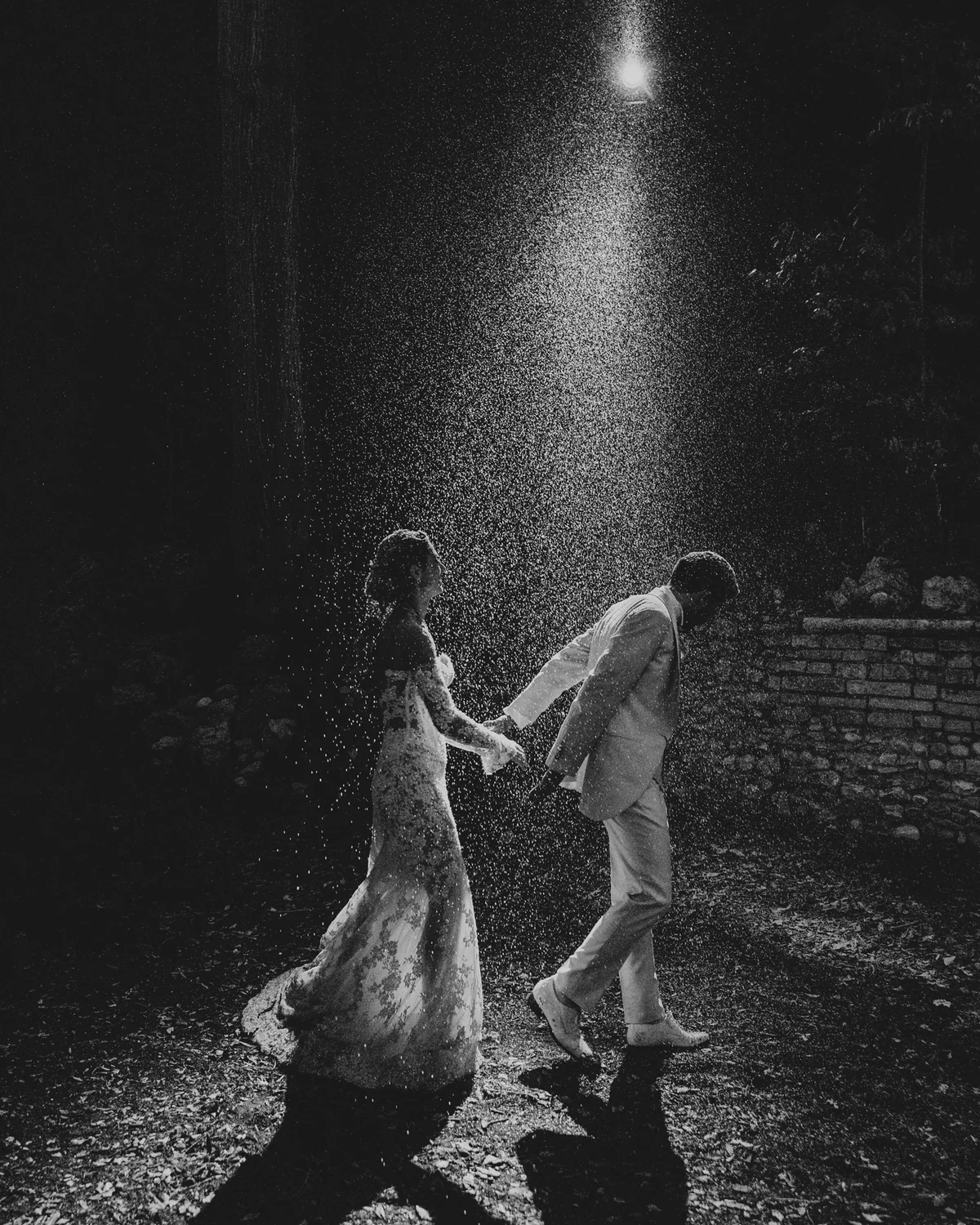 A couple hand in hand in the rain at night, in black and white
