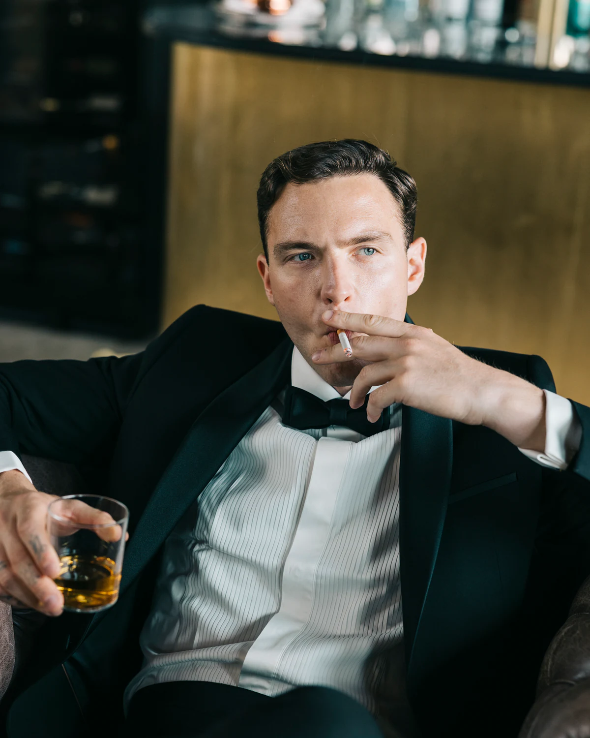 A man in a tuxedo holding a glass of whisky