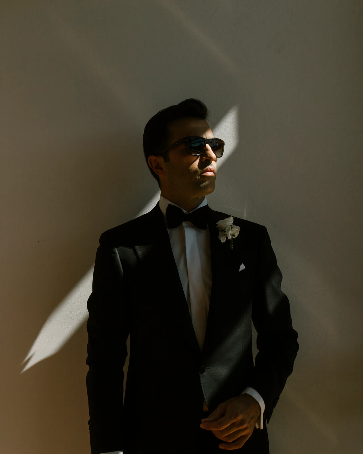 A man in a tuxedo and sunglasses standing in a shaft of light
