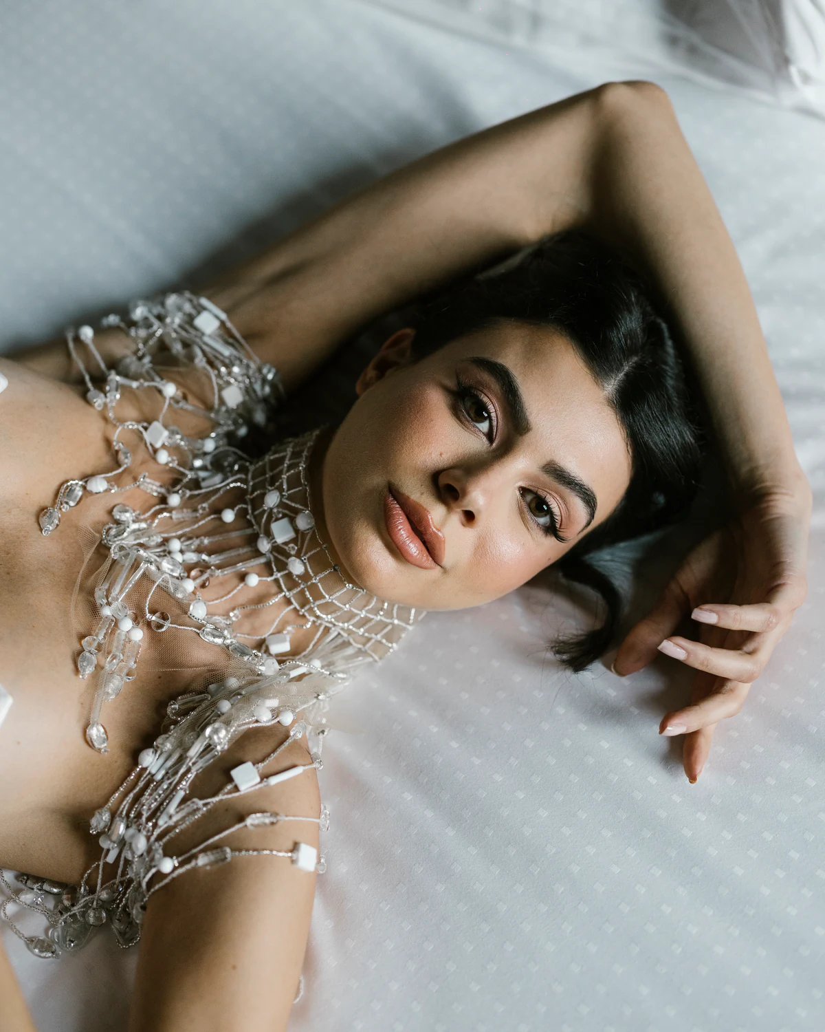 A woman lying on a bed, wearing a crystal neckpiece