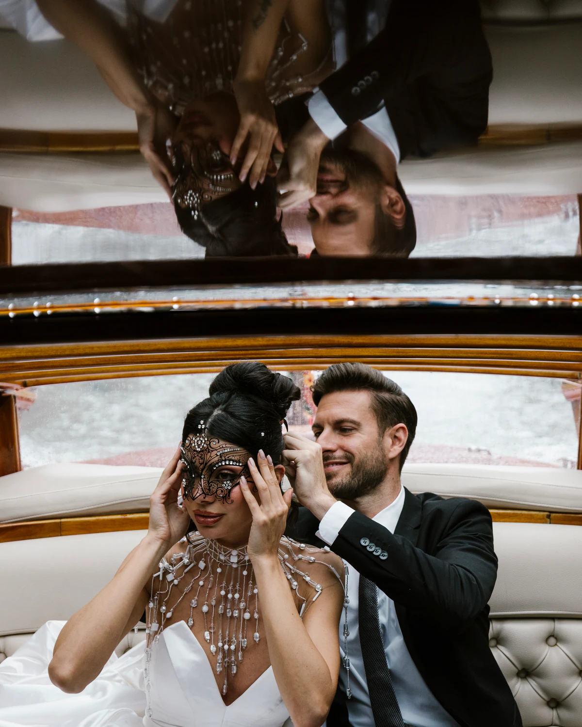 A couple inside a Venetian motorboat, she in a lace mask, reflected in the ceiling