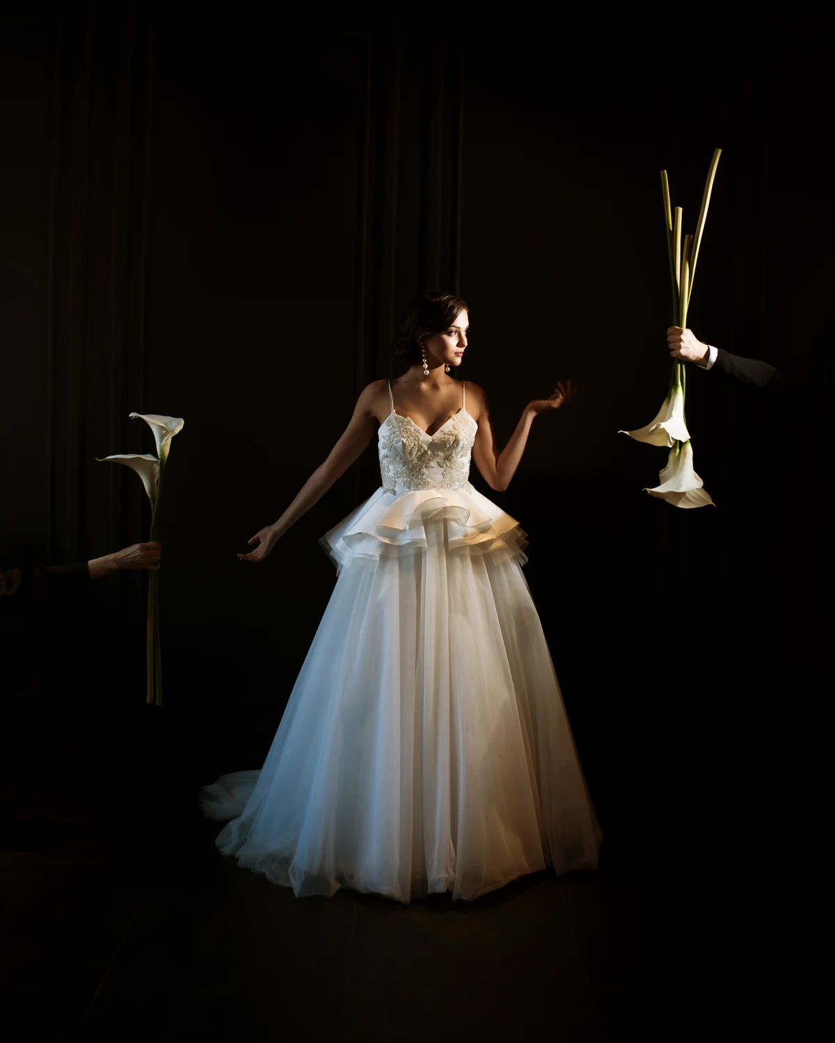 A bride in the dark, with calla lilies held out to her by two hands entering the frame