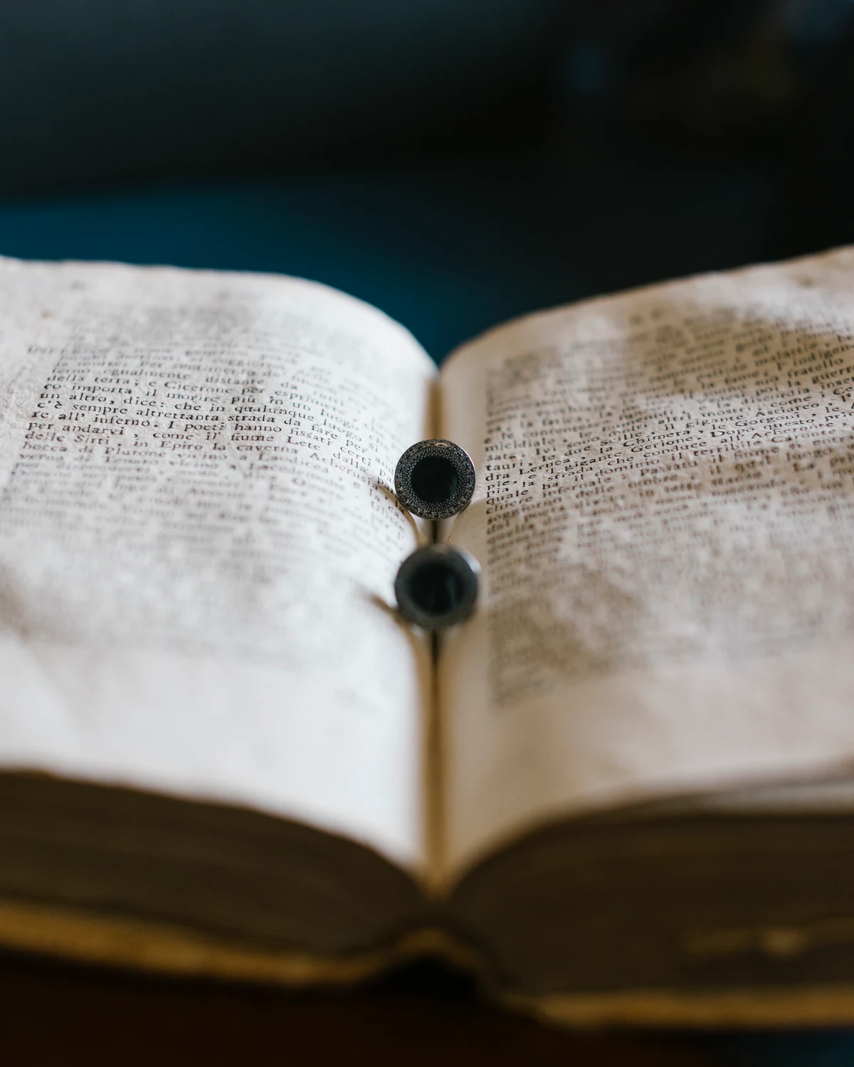 An antique book open on a table, with a pair of cufflinks resting on its pages