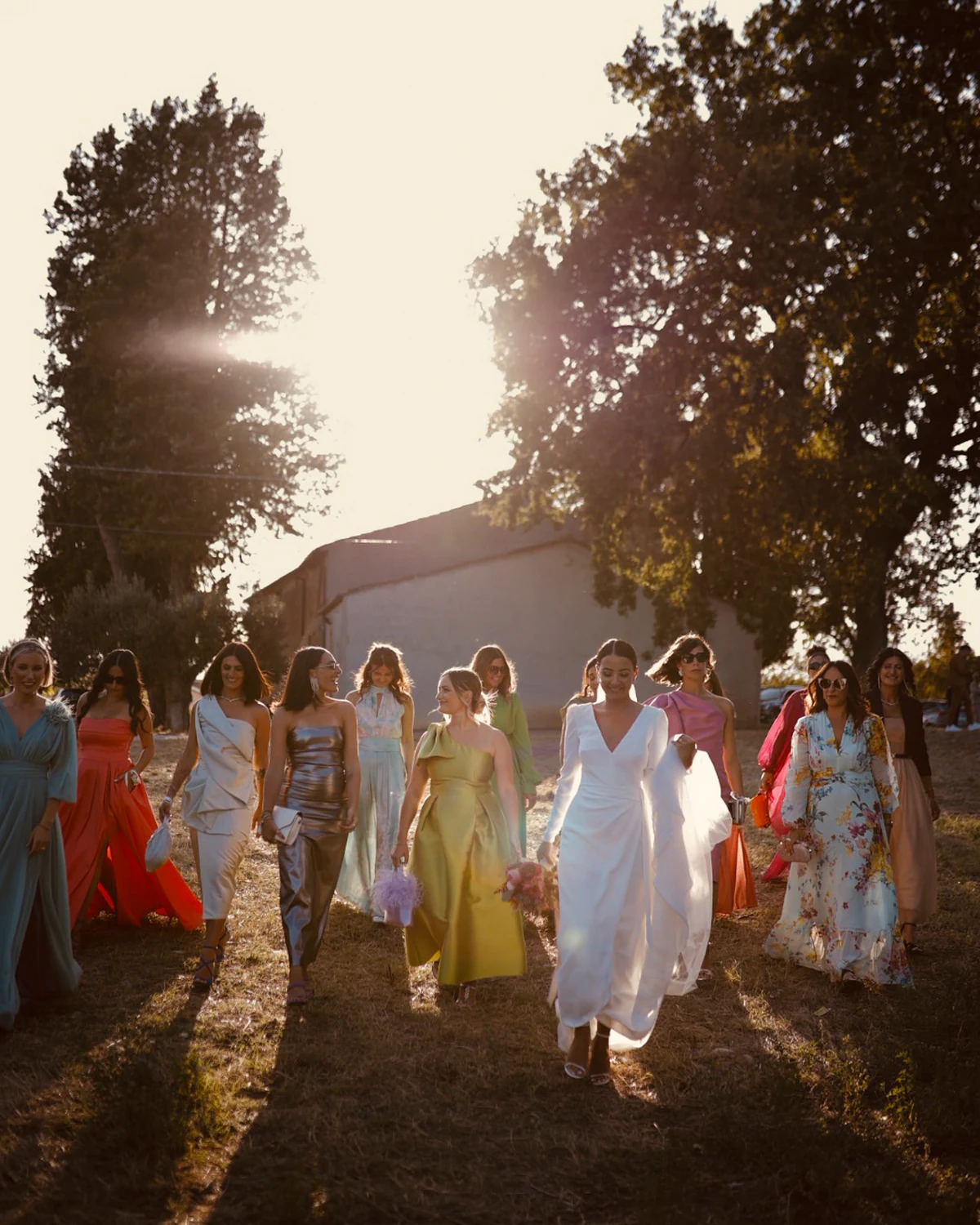 The bride walking through the fields in the evening light, surrounded by her guests