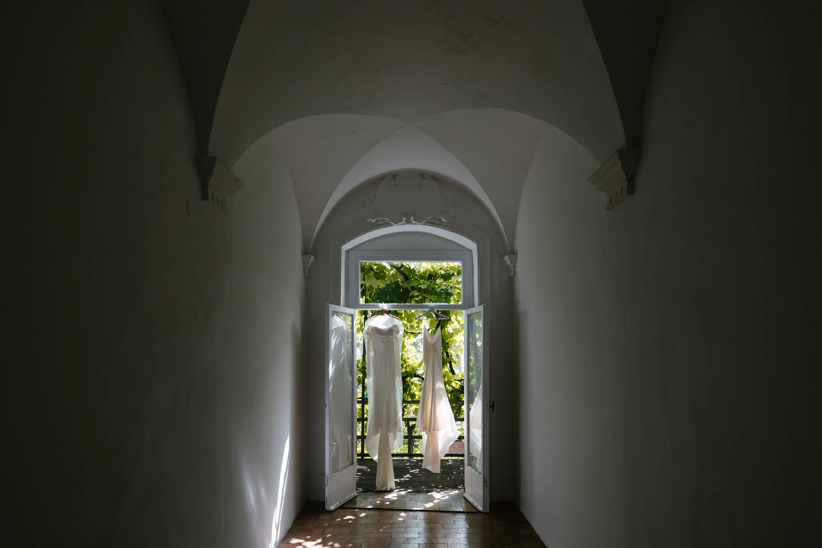 Two dresses hanging in an open doorway at the end of a vaulted corridor