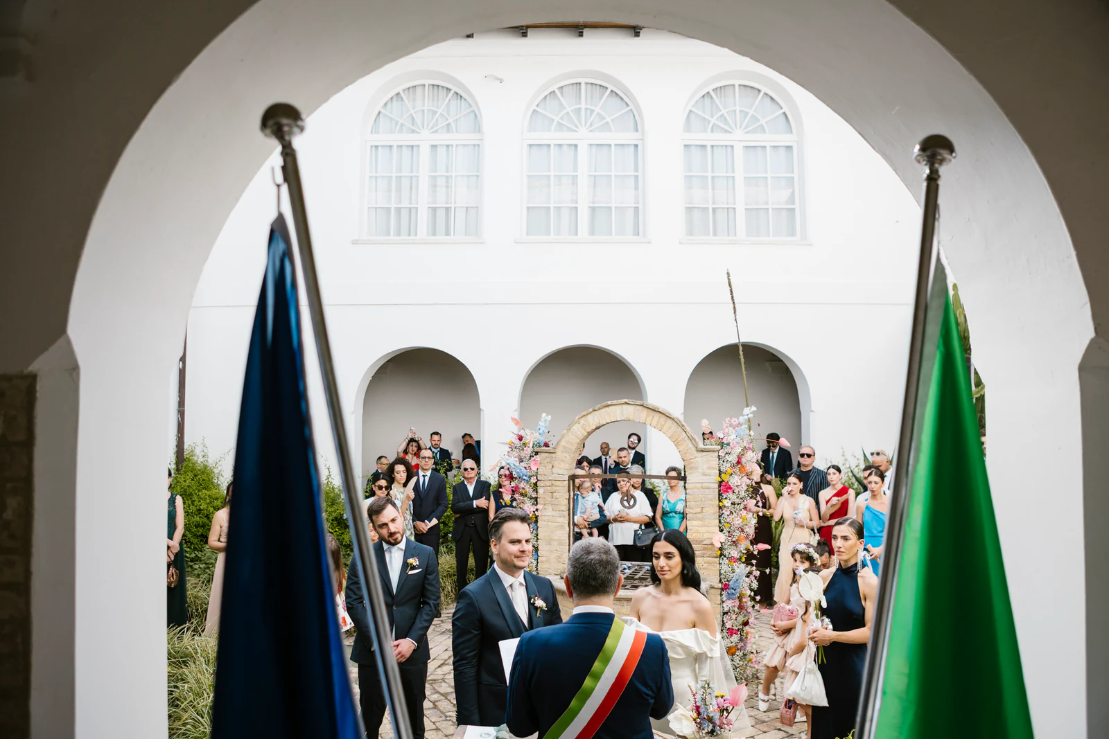 The ceremony in the cloister, seen through an arch between two flags