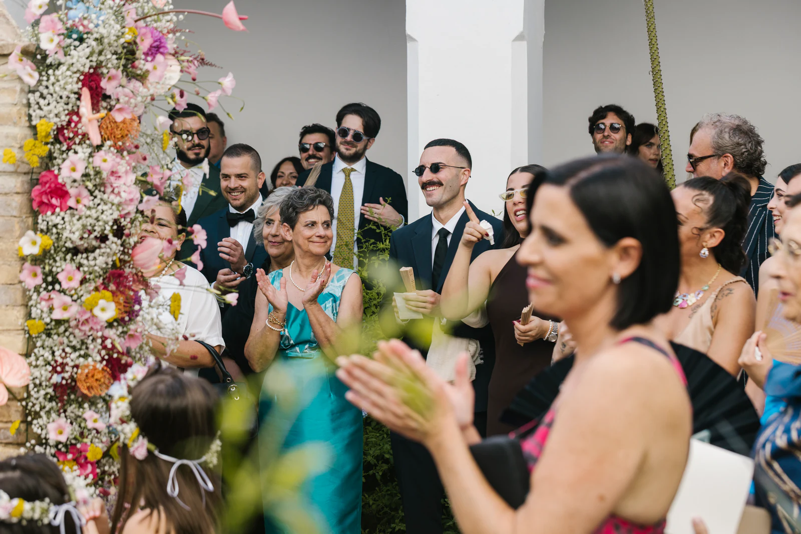 Guests applauding beside a wall of flowers