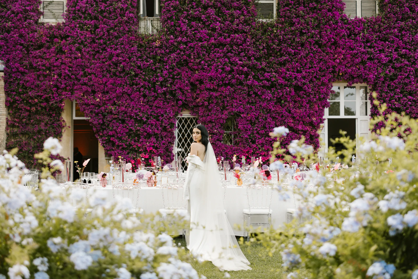 The bride beside the long table, under a wall of bougainvillea
