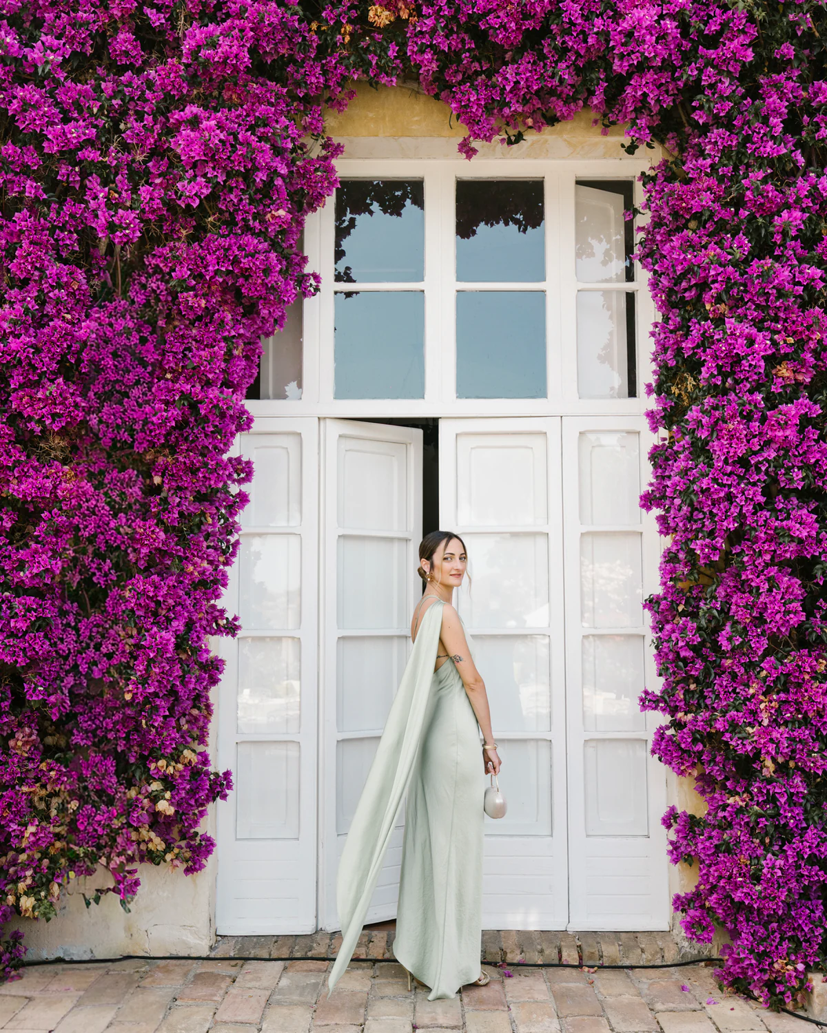 A guest in a pale green dress at a doorway framed with bougainvillea