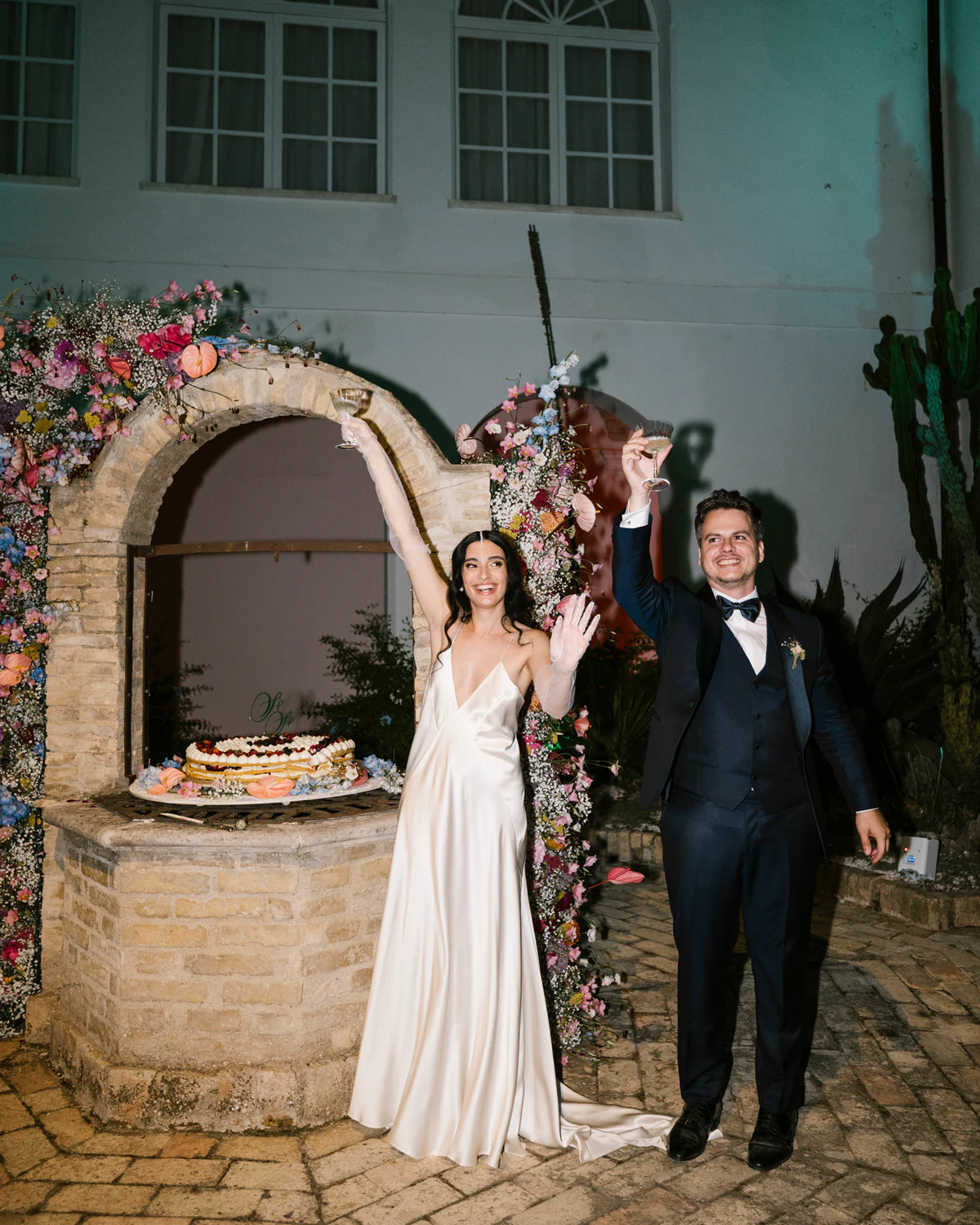 The couple beside a stone well decorated with flowers, at dusk