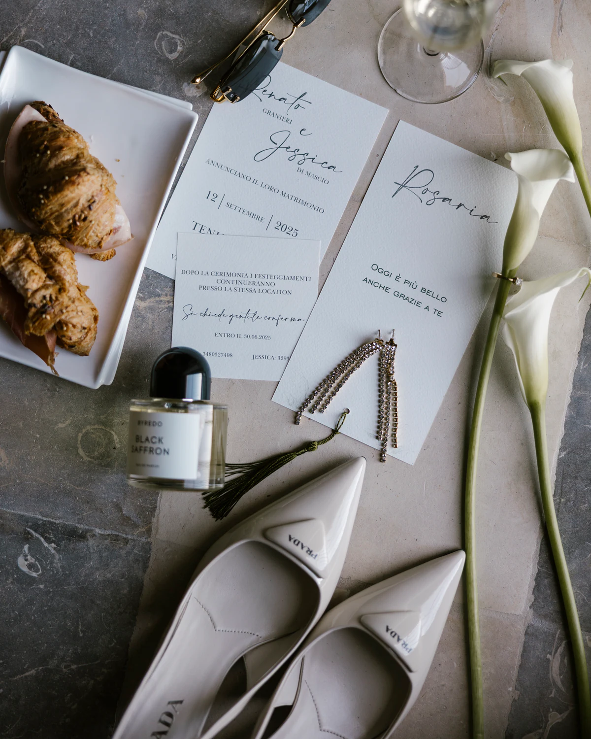 The invitations, calla lilies, perfume and the bride's shoes on a table