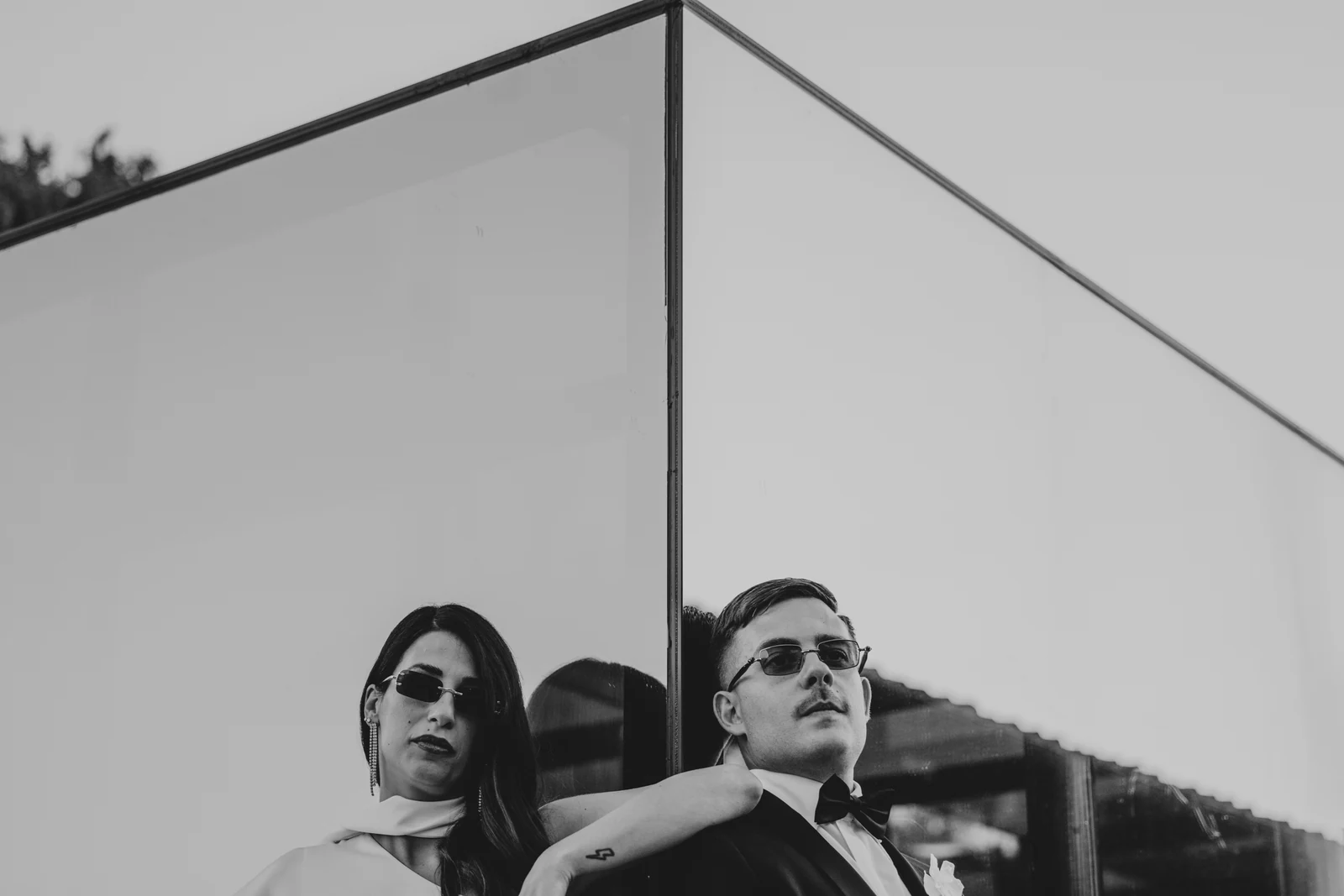 The couple in sunglasses in front of a glass wall