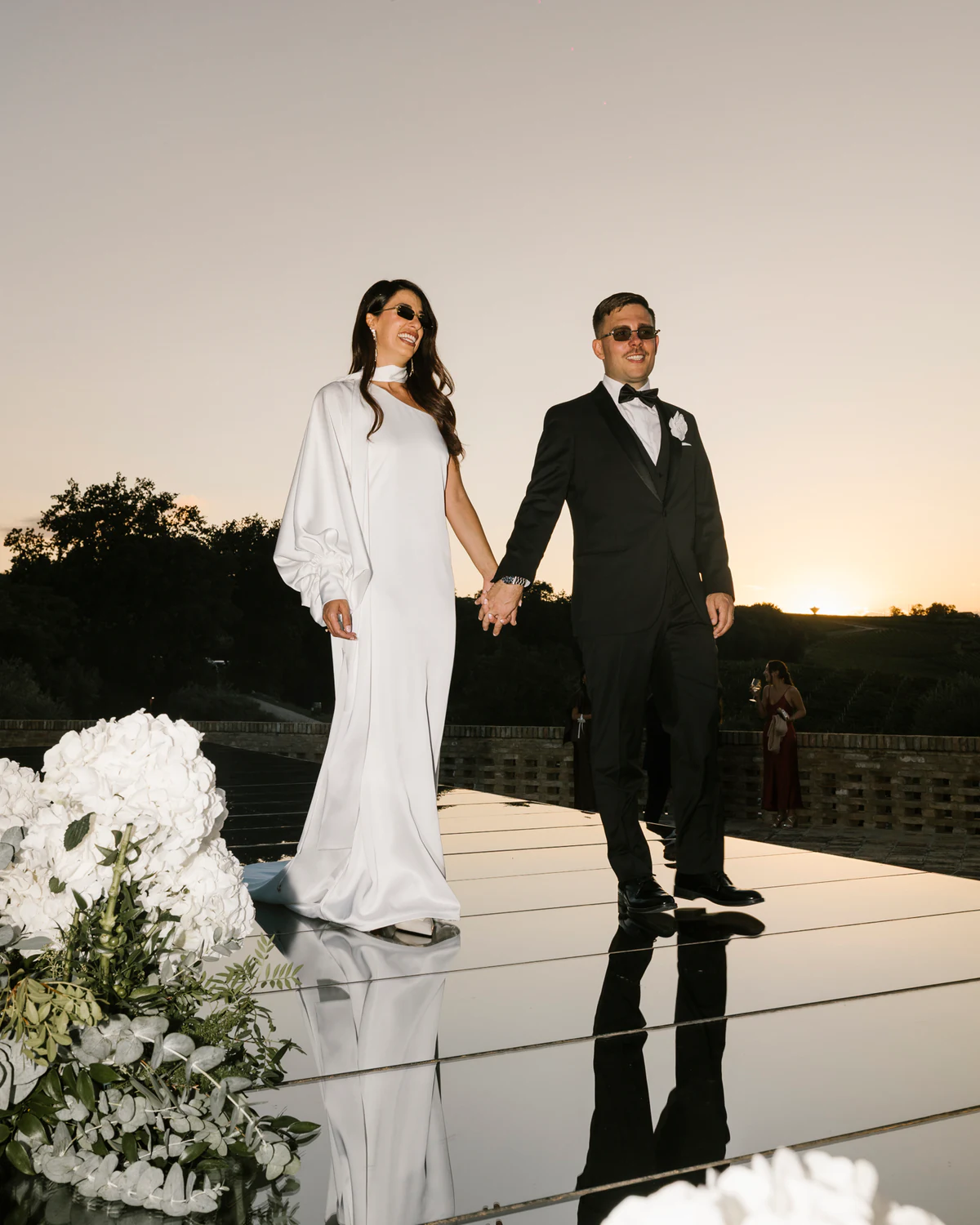 The couple walking hand in hand on a mirrored floor at sunset