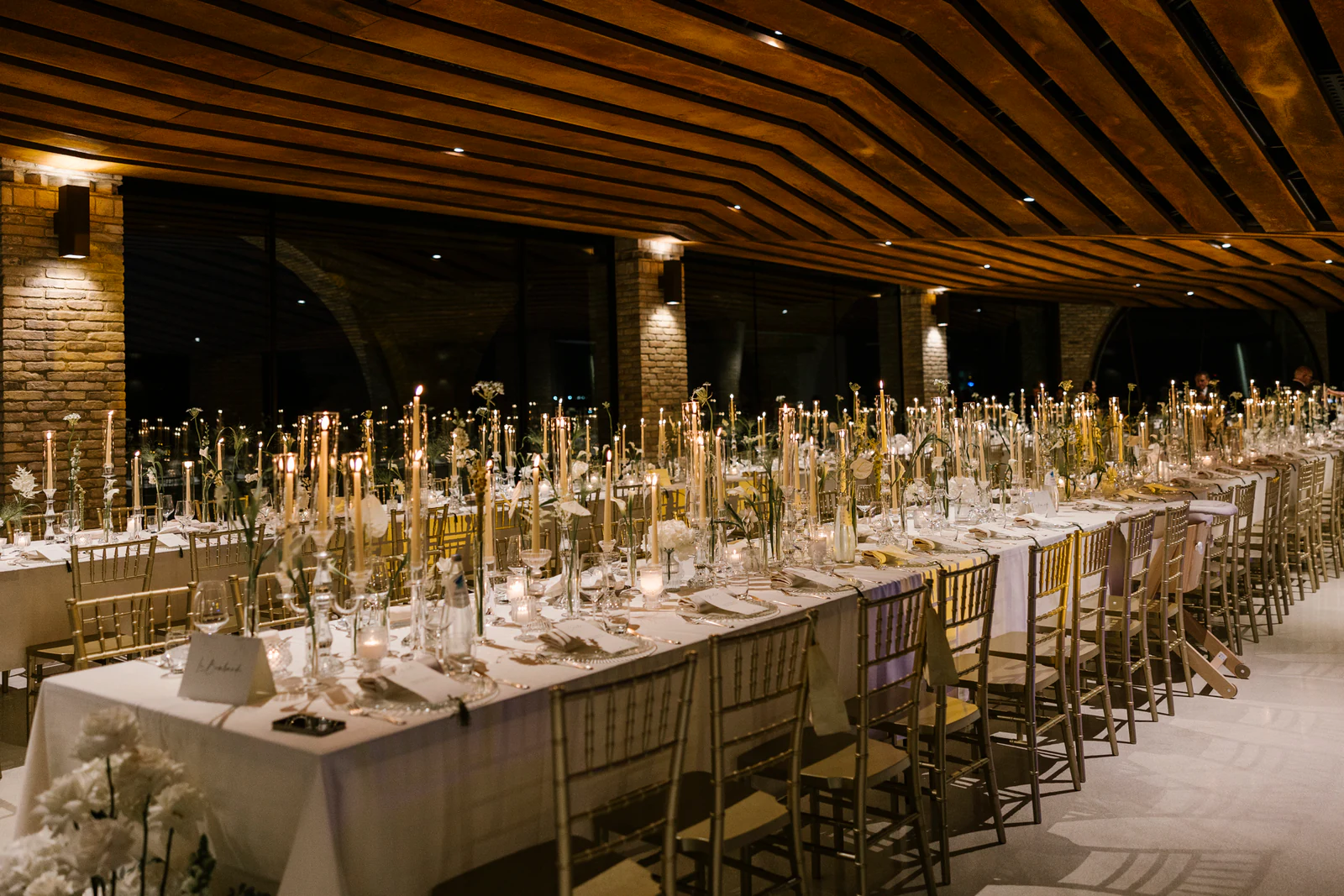 The long dinner table under a wooden roof, lit by candles