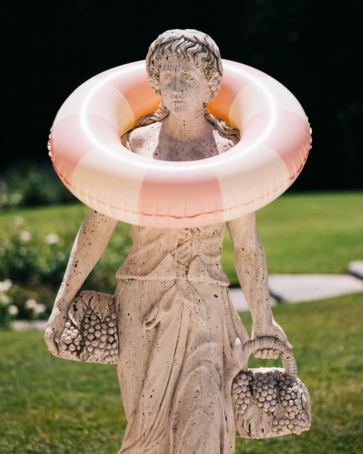 A garden statue wearing a pink-and-white pool ring