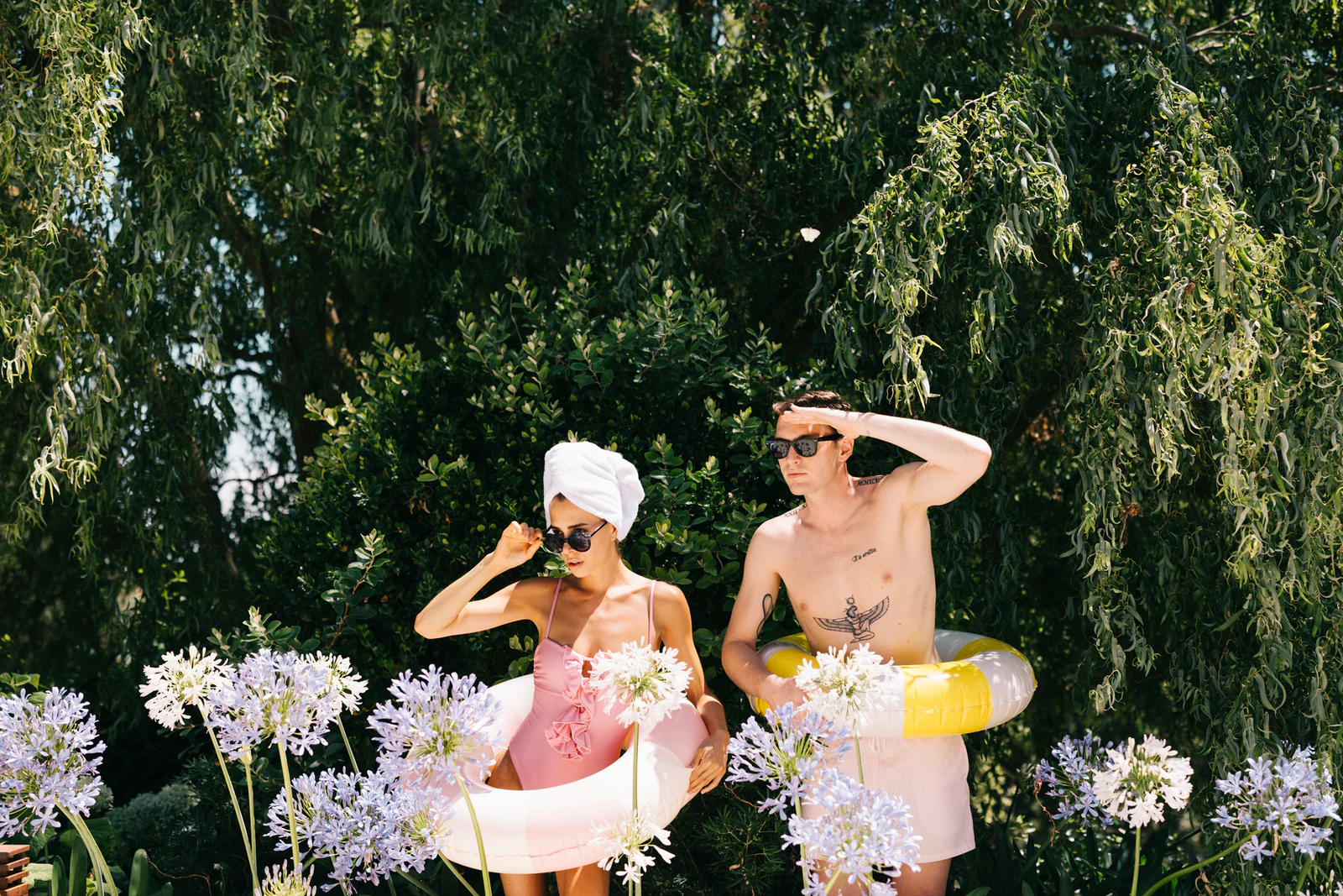 The couple among agapanthus in the garden, with pool rings and towels