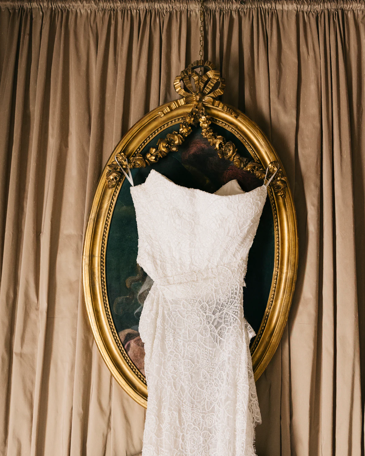 The wedding dress hanging in front of a gilded mirror