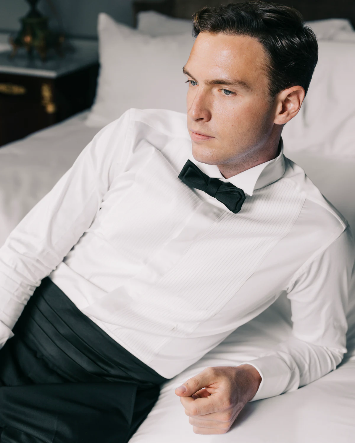 The groom in a white shirt and bow tie, lying on the bed