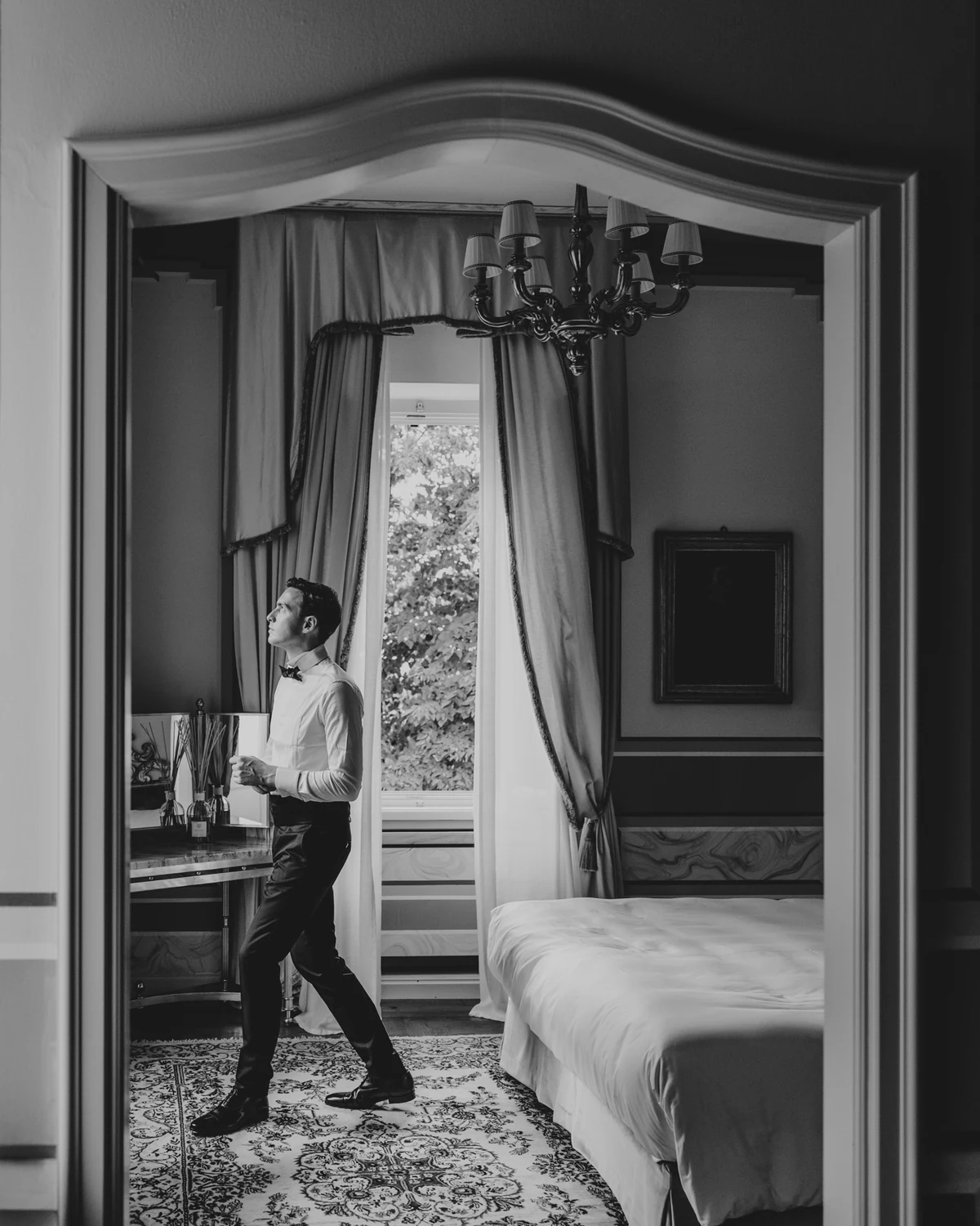 The groom crossing a period bedroom with a chandelier