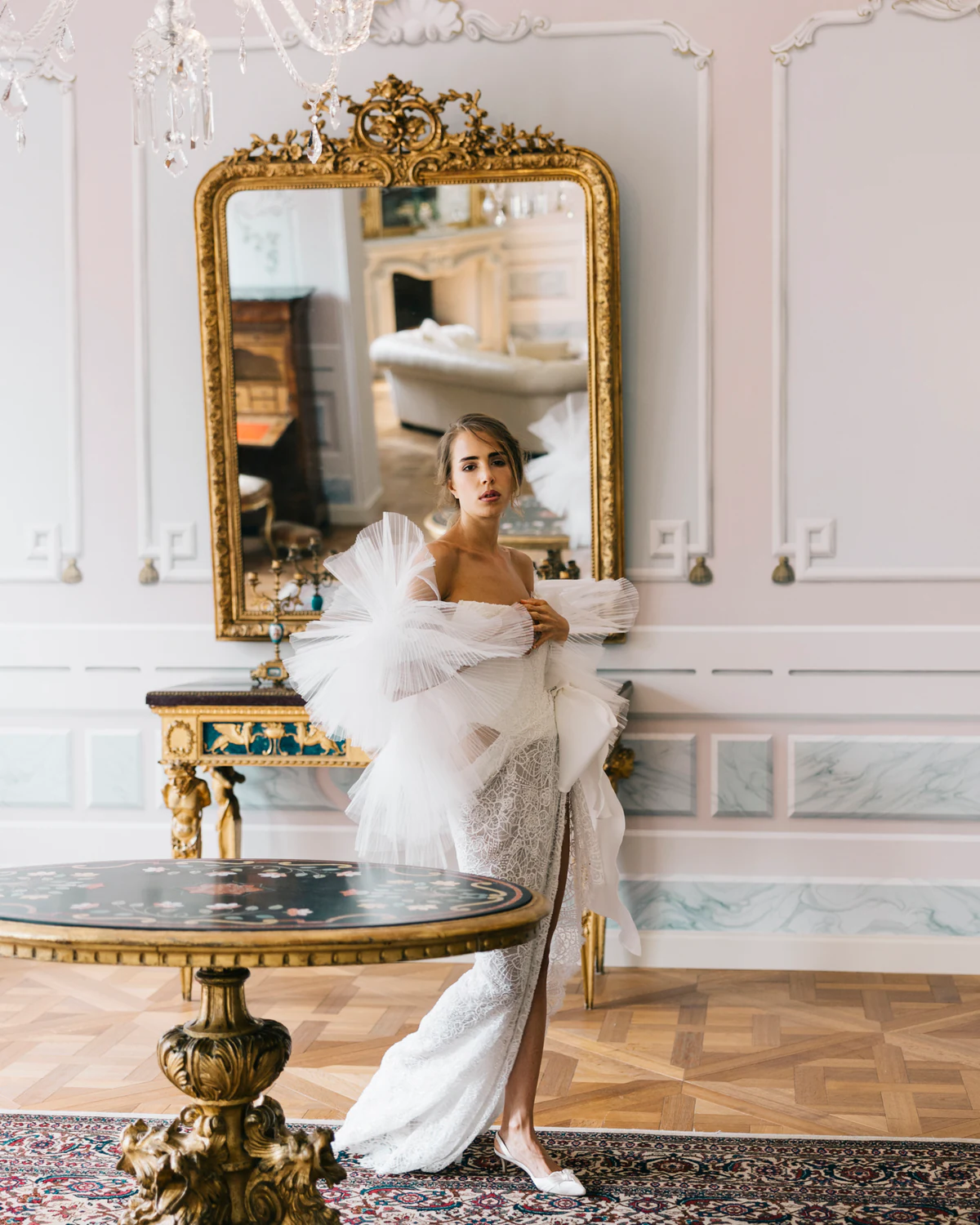 The bride in a feather wrap beside a gilded console