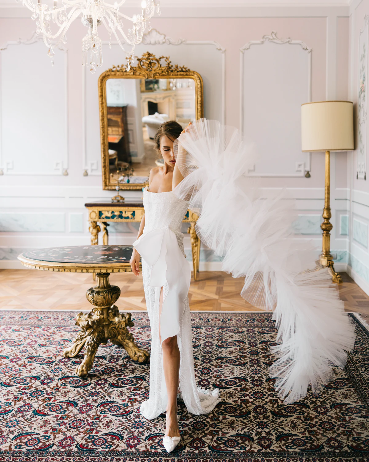 The bride with a feathered train in a room with a gilded mirror