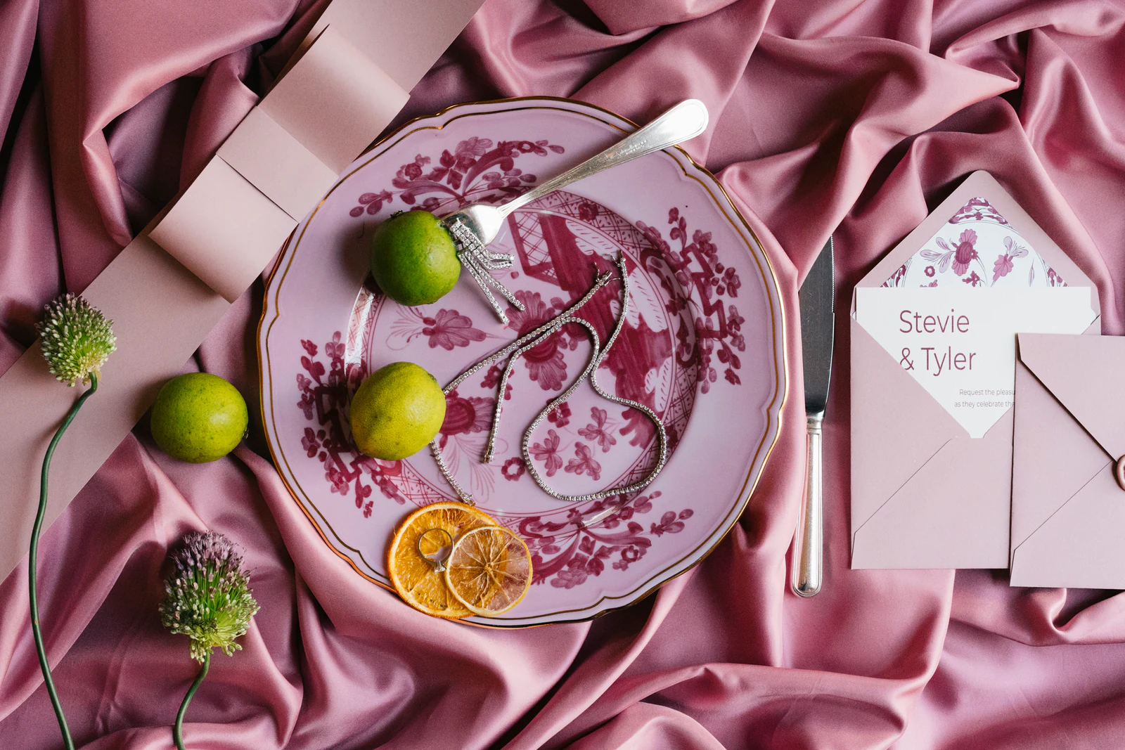A pink table setting with limes, silk and invitations