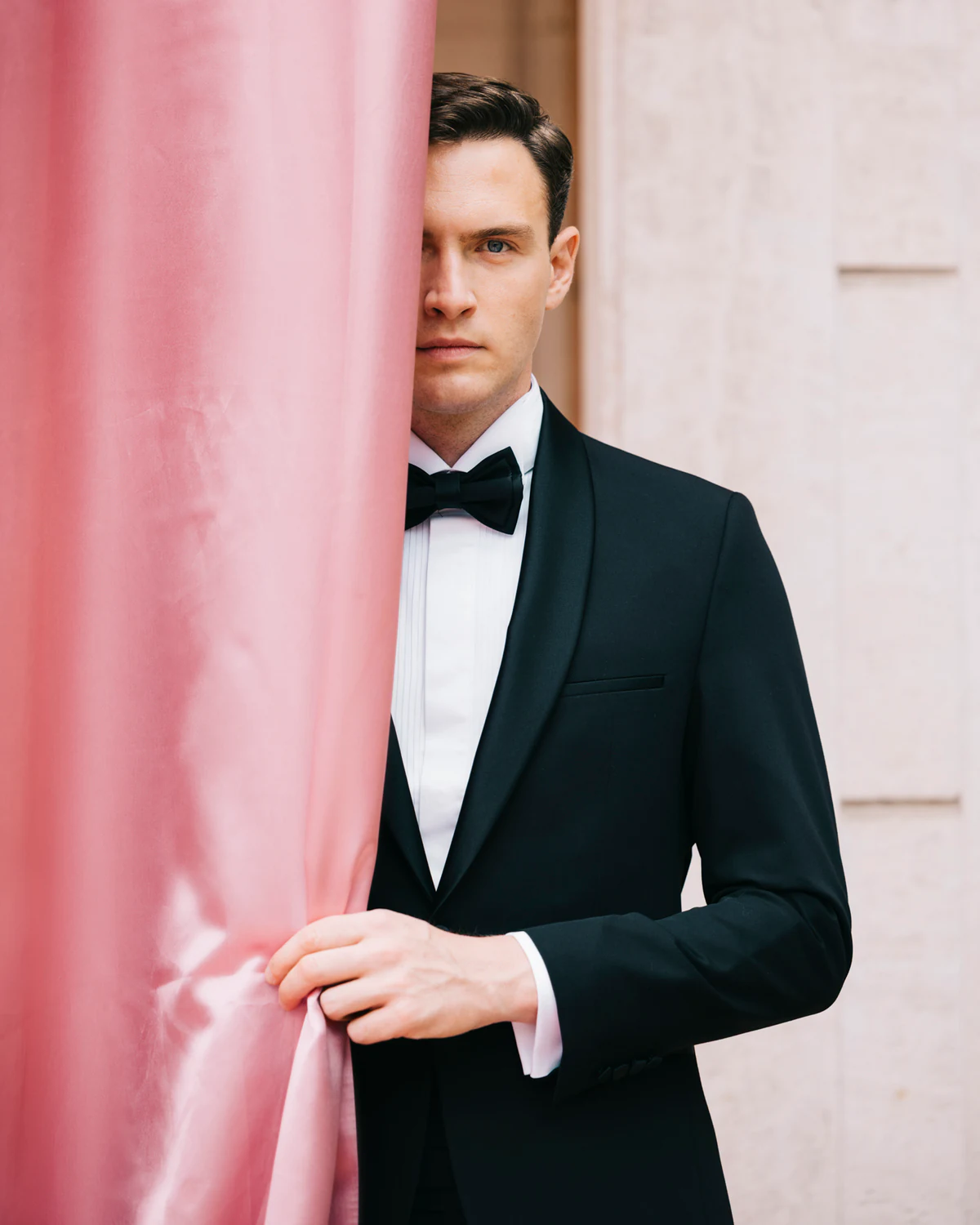 The groom in a tuxedo beside a pink curtain