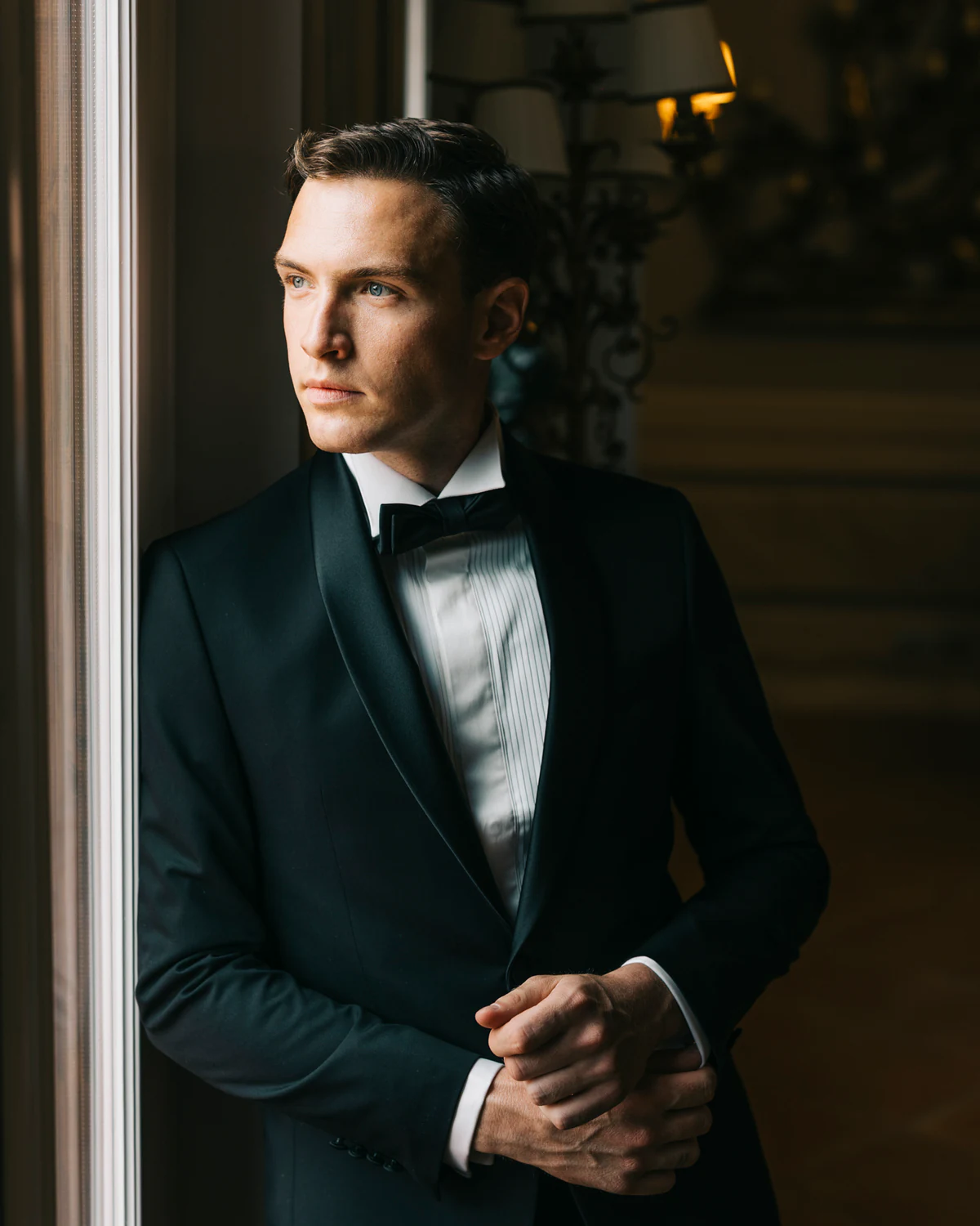 The groom in a tuxedo by a window