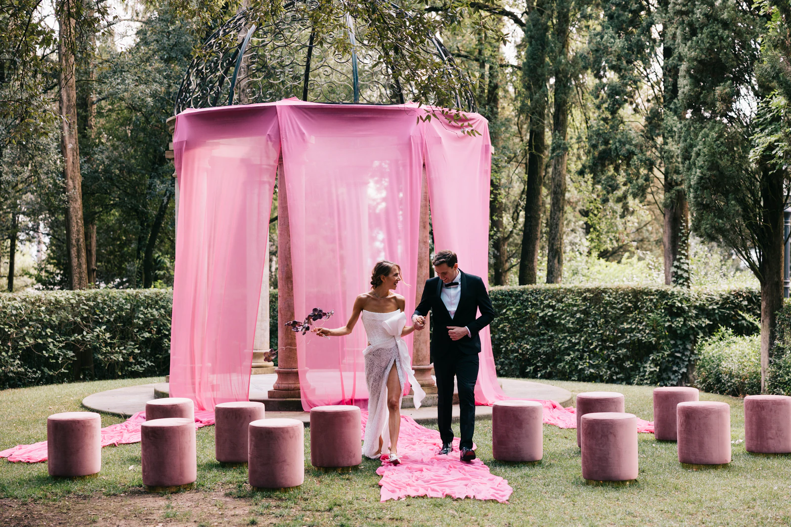The couple walking out of the pink gazebo in the garden