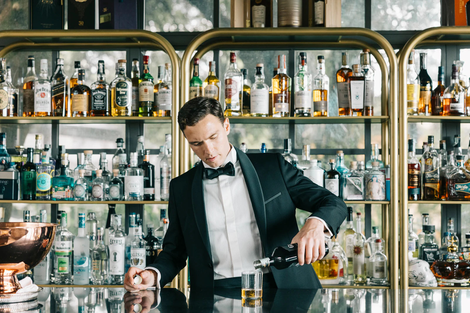 The groom pouring a drink behind a bar full of bottles