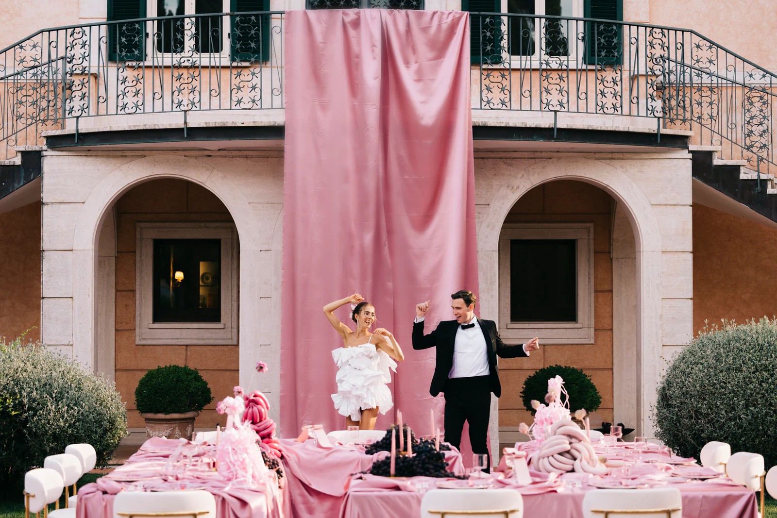 The couple dancing at the long pink table in front of the villa