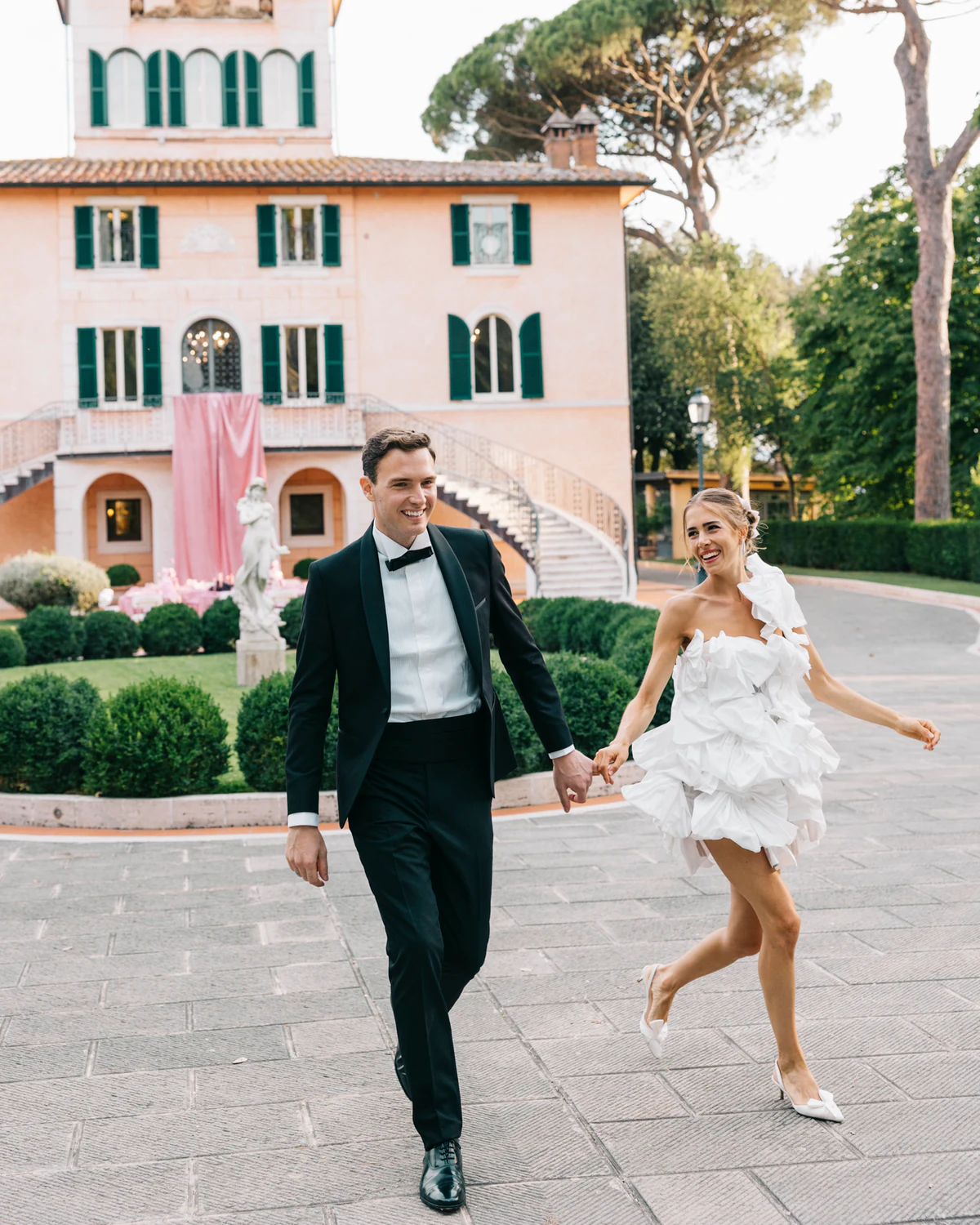 The couple running hand in hand in front of the villa