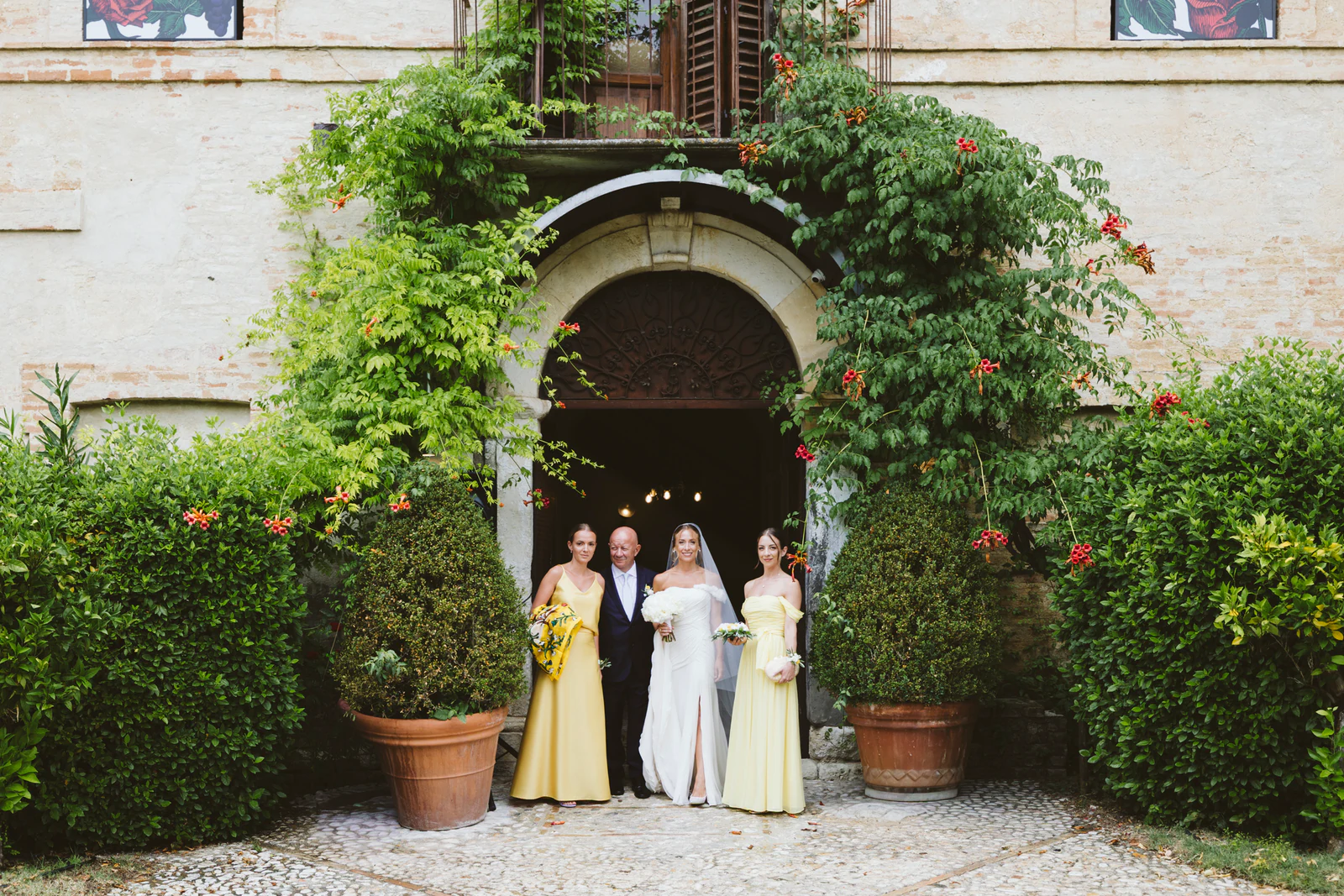 The bride with her bridesmaids in yellow in front of an arched doorway